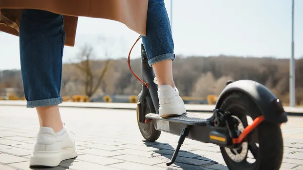 Personne en jean et baskets blanches sur une trottinette électrique en ville